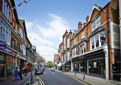 Town-centre street decorated with bunting above terraced shops under a blue sky