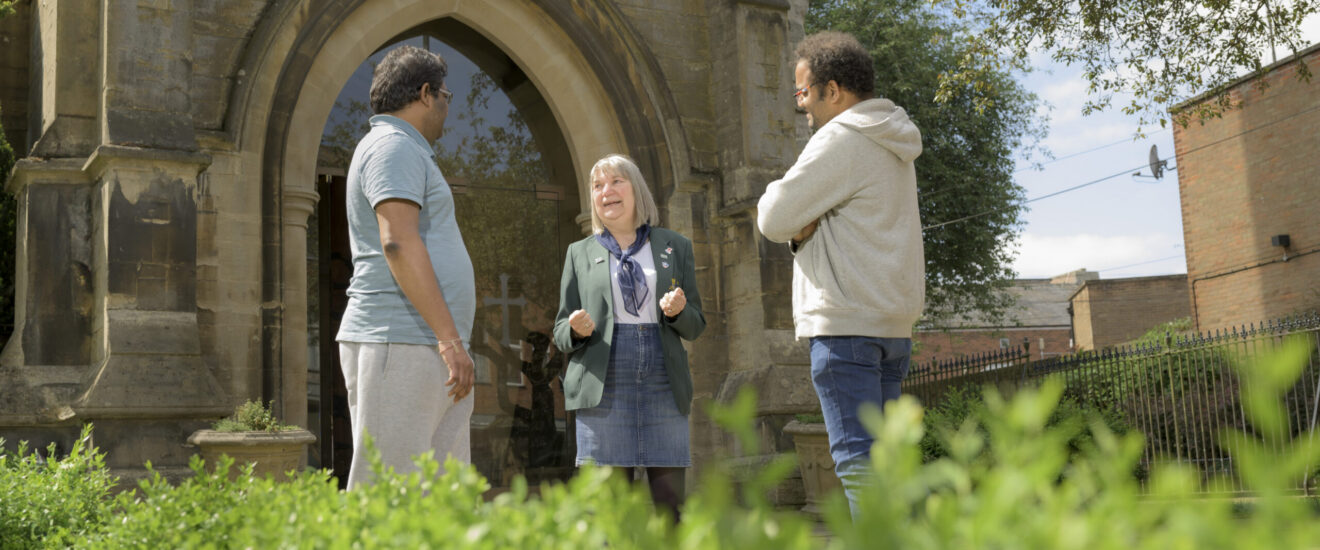 Small group chatting outside a stone church with a Gothic arched doorway on a heritage walking tour