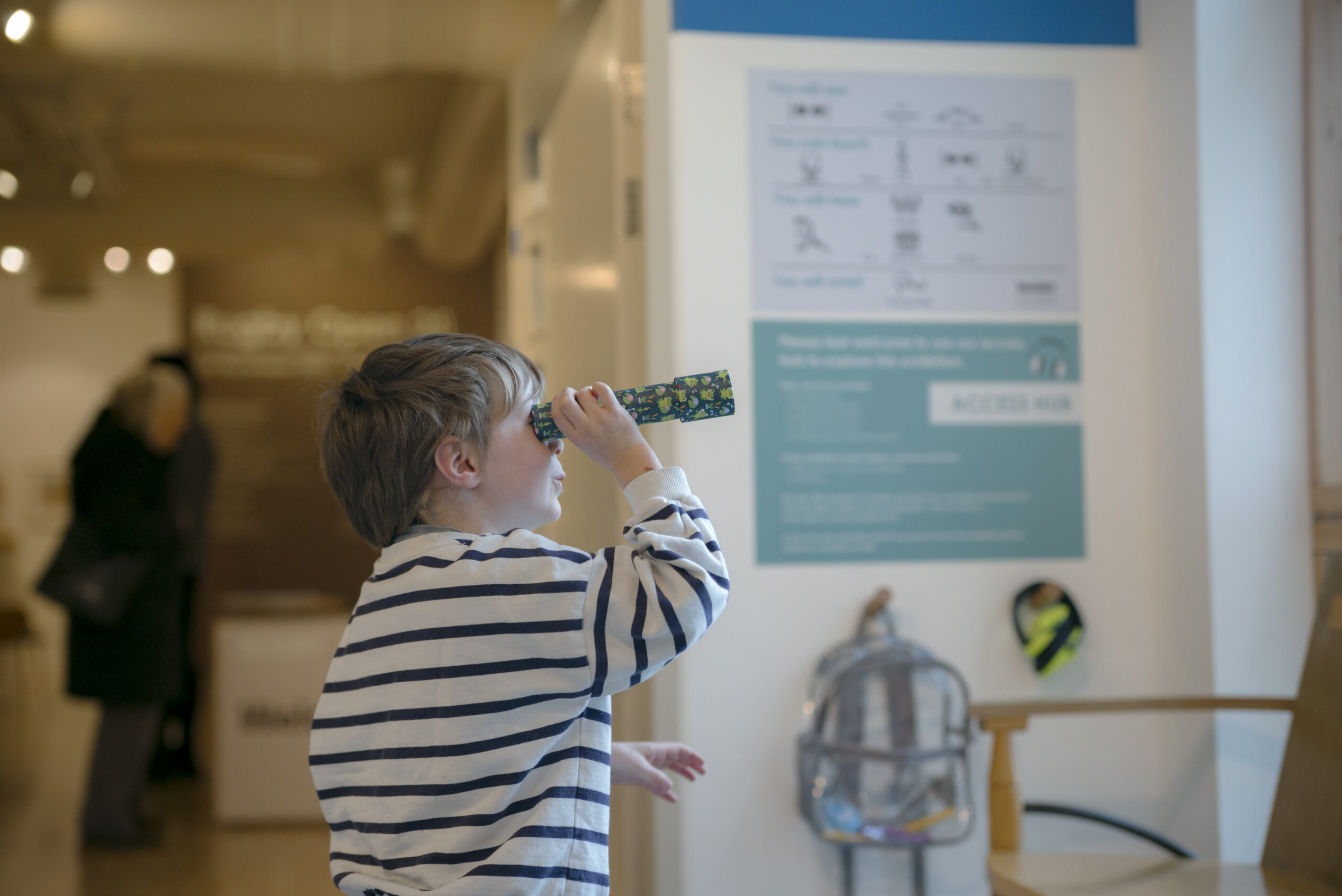 Child holding a small telescope up to their eye inside the light filled interior of the art gallery and library
