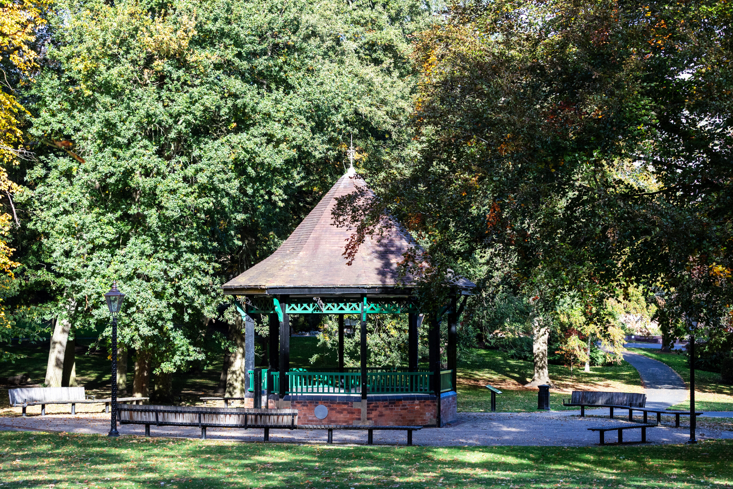 Park bandstand with a tiled roof surrounded by mature green trees