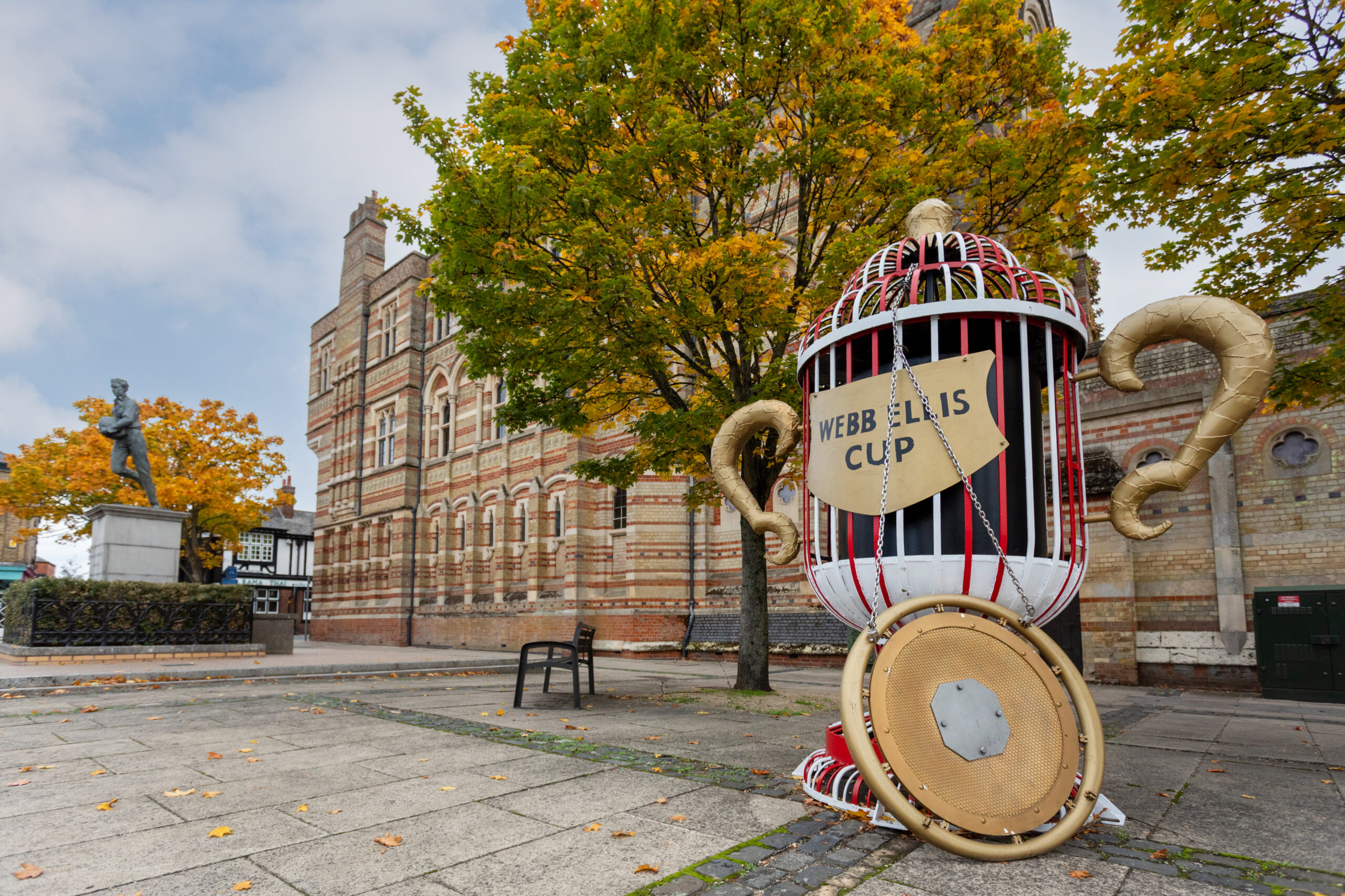 Rugby School's Victorian Gothic buildings behind an oversized Webb Ellis Cup statue, in autumn