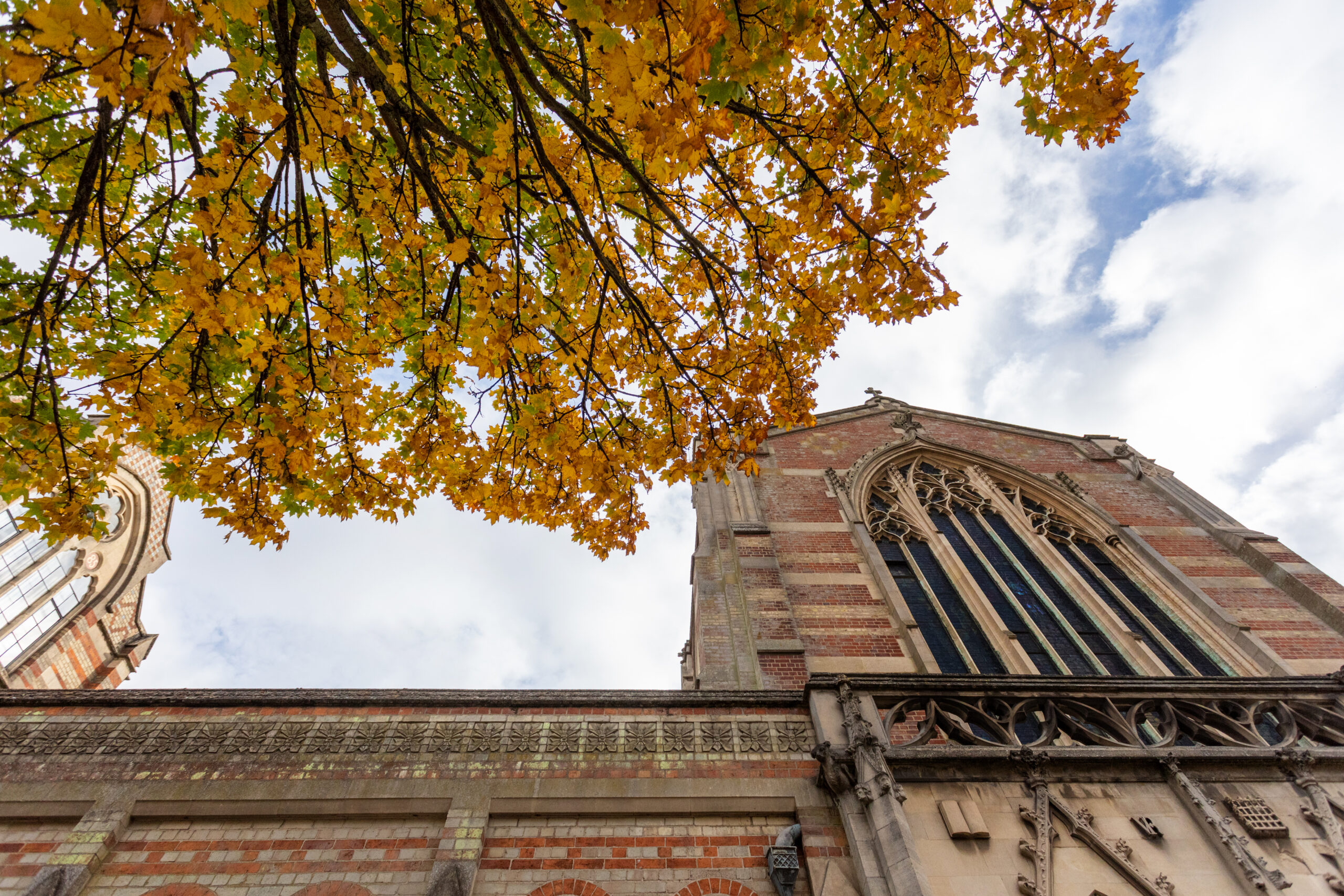 Gothic-style church façade framed by colourful autumn foliage against a partly cloudy sky