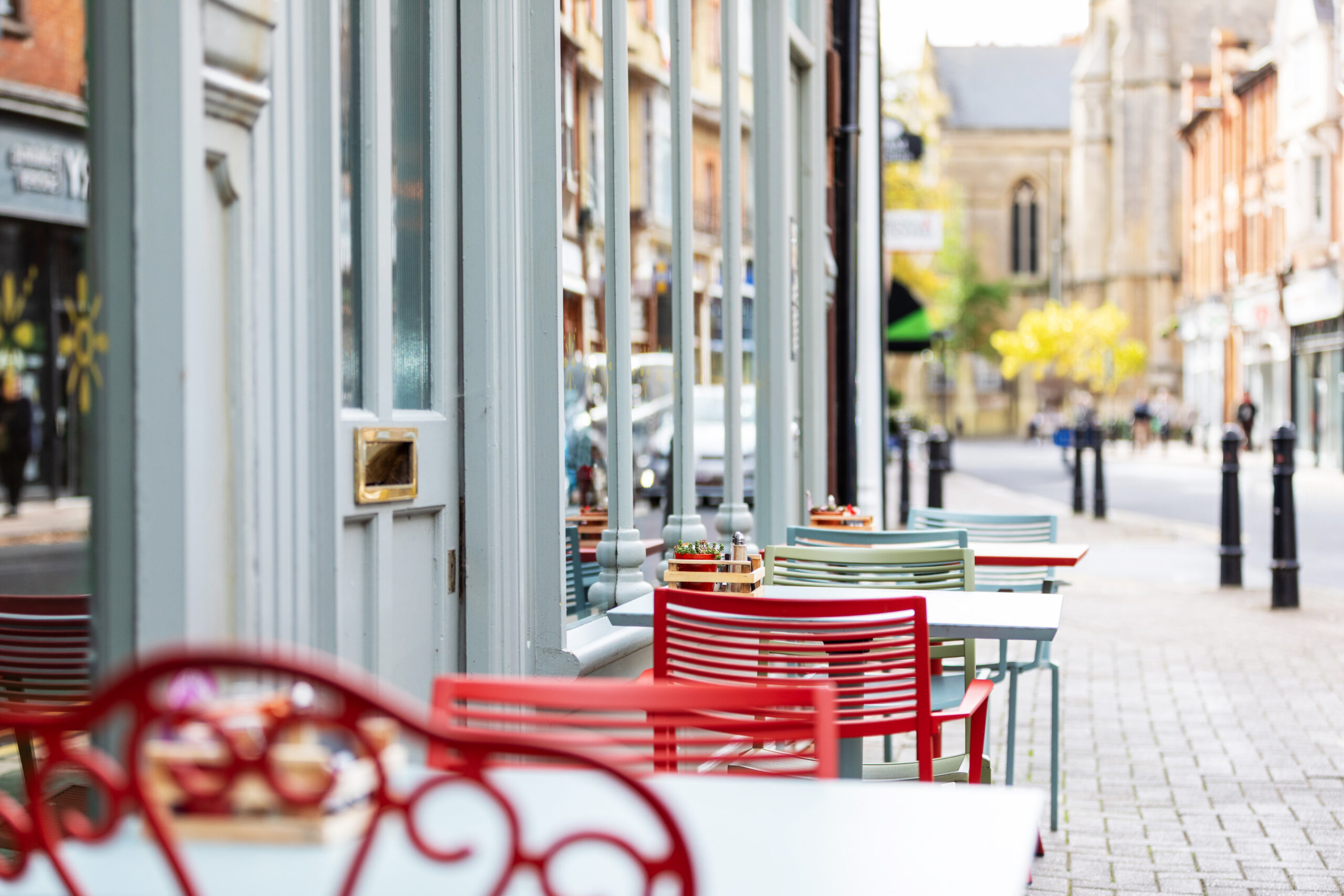 Outdoor dining tables in front of a restaurant, looking up a street in rugby town centre on a sunny autumnal day