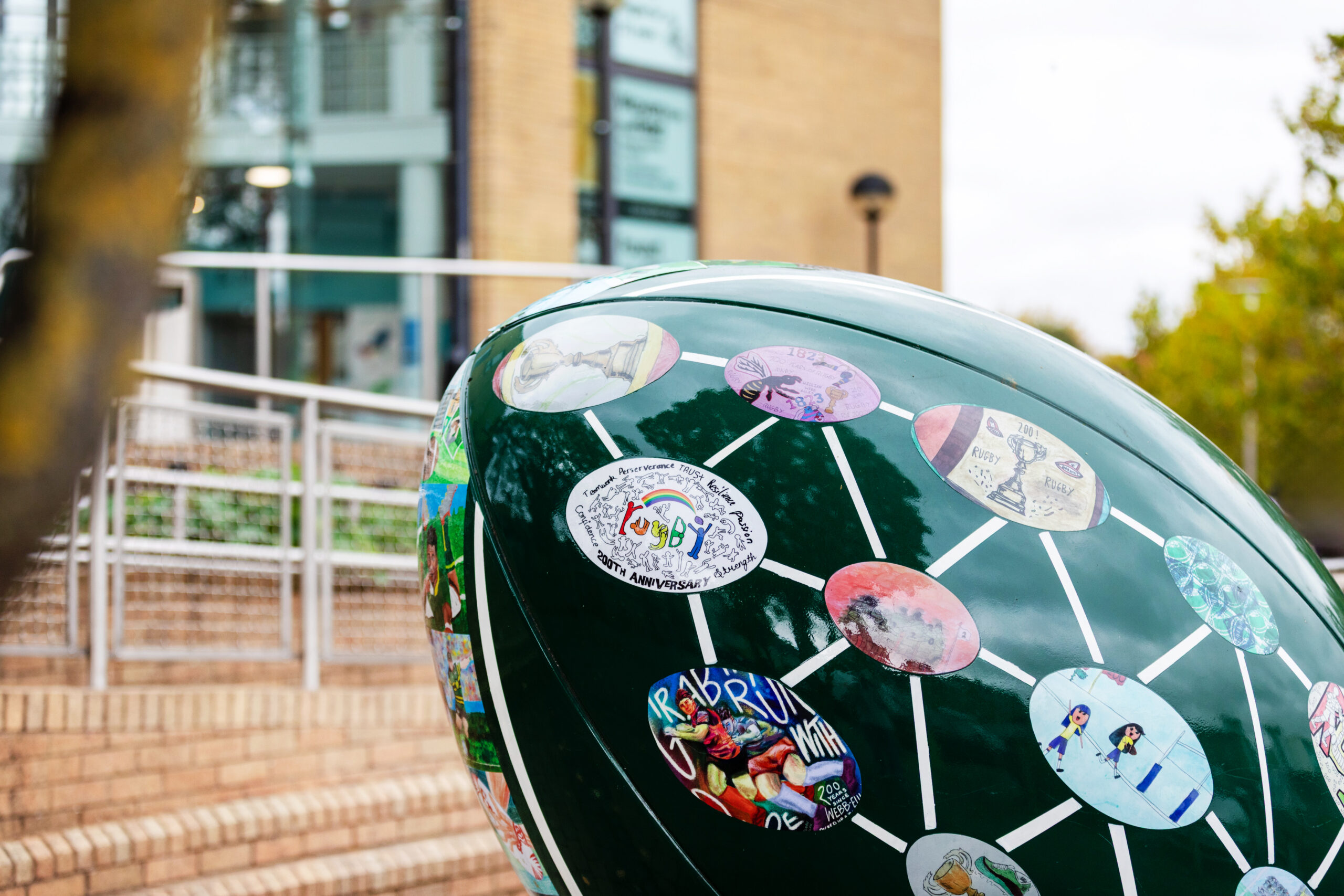 Painted rugby ball sculpture featuring local artwork and illustrations outside a town centre building