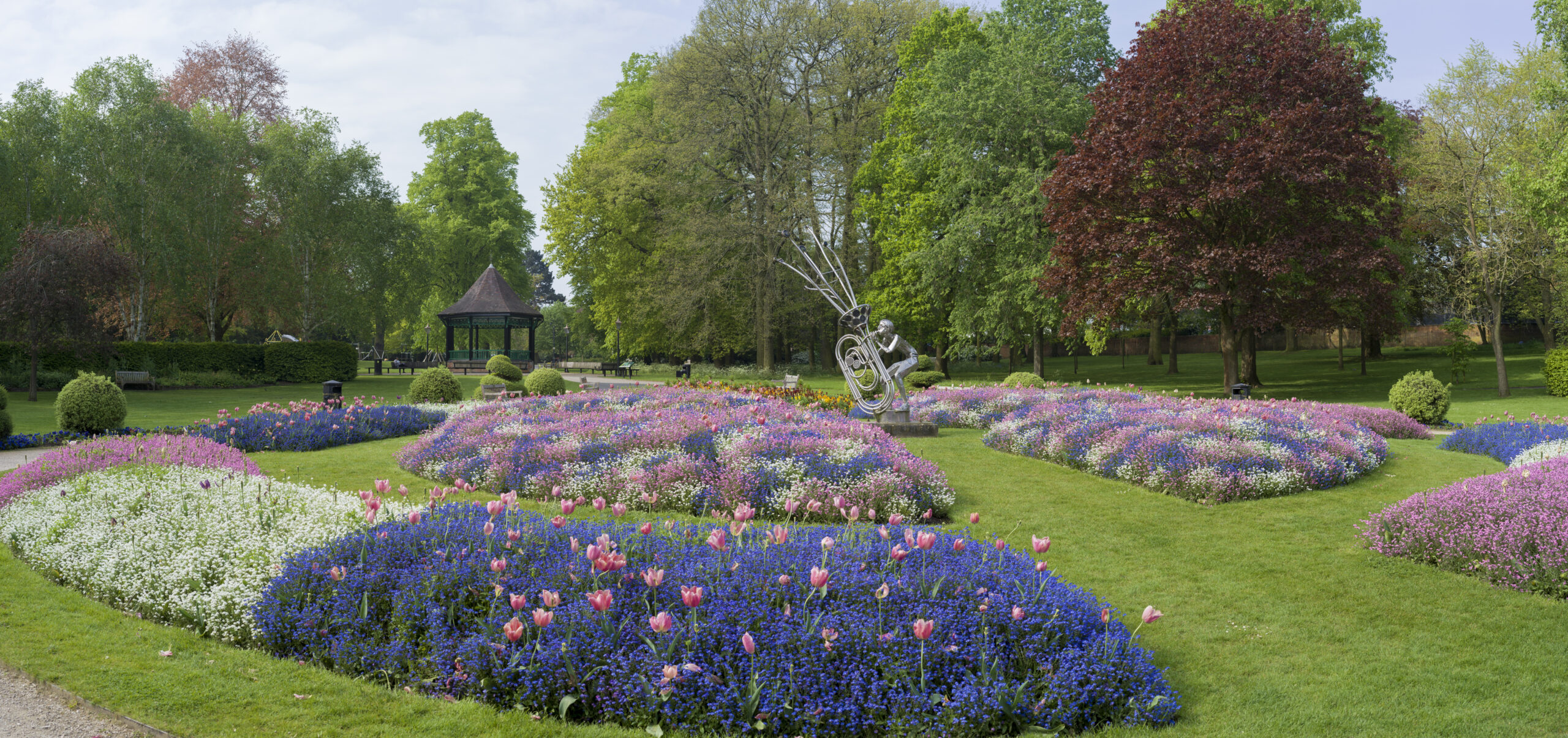 Colourful formal flower beds, lawns, a bandstand and a sculpture in Caldecott Park