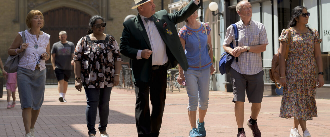 Guide in a boater hat leading a group of visitors on a walk through the pedestrianised town centre