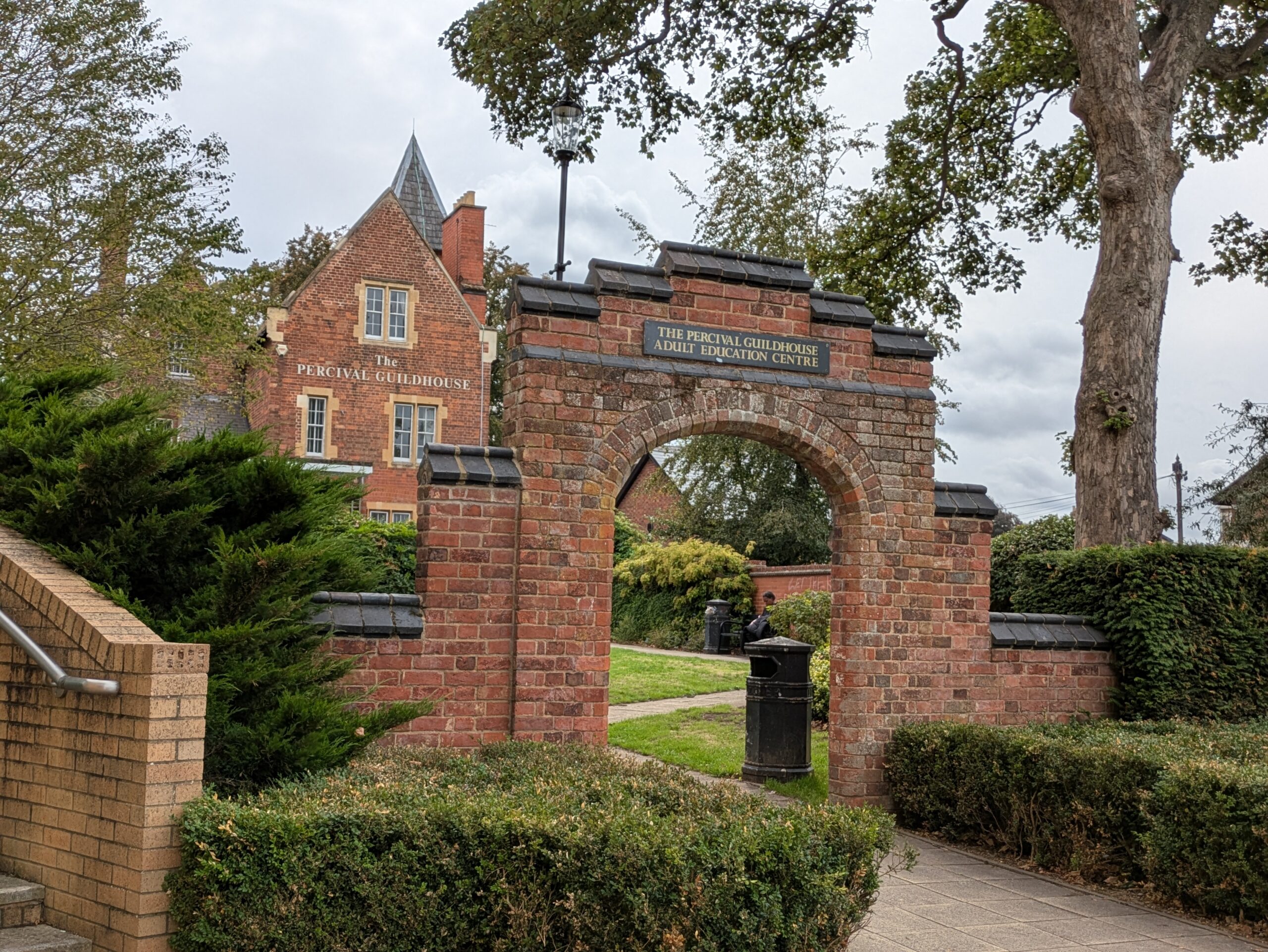 an archway to a garden with a red brick building in the background.