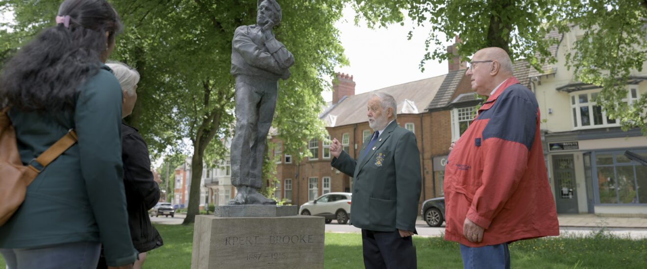 A group of people in a park discussing a sculpture of a man.