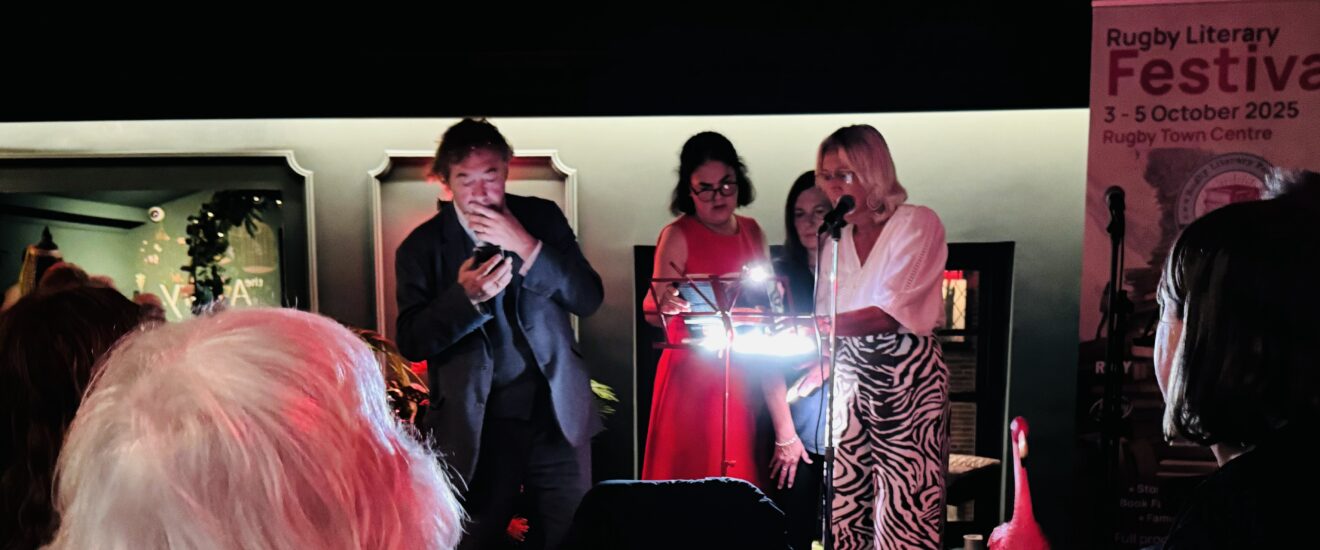 Group of people in a dimly lit space, some are seated and some are stood speaking.
