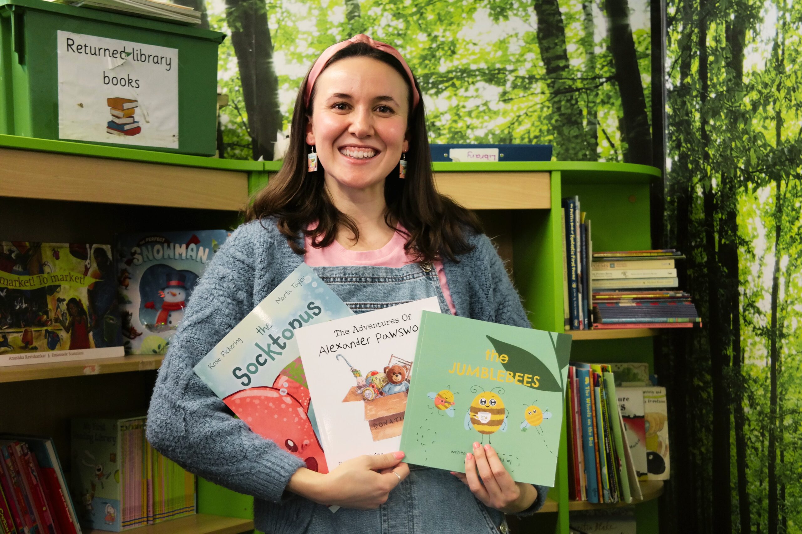 author holding books with trees in the background