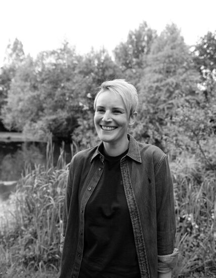 A woman stood by a lake smiling.