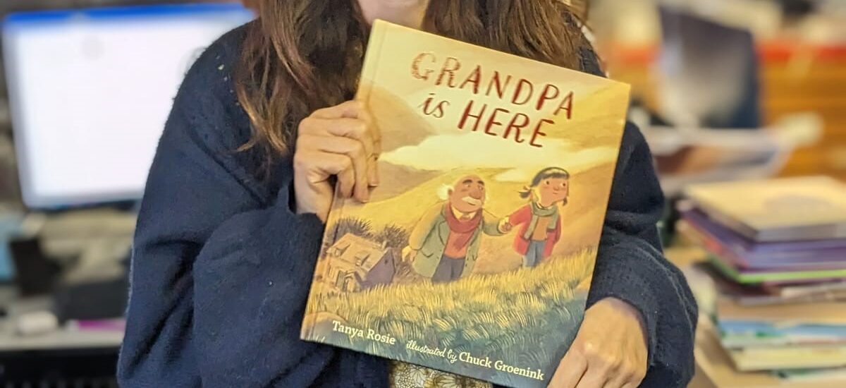 woman holding a childrens book with people walking up a hill on the cover
