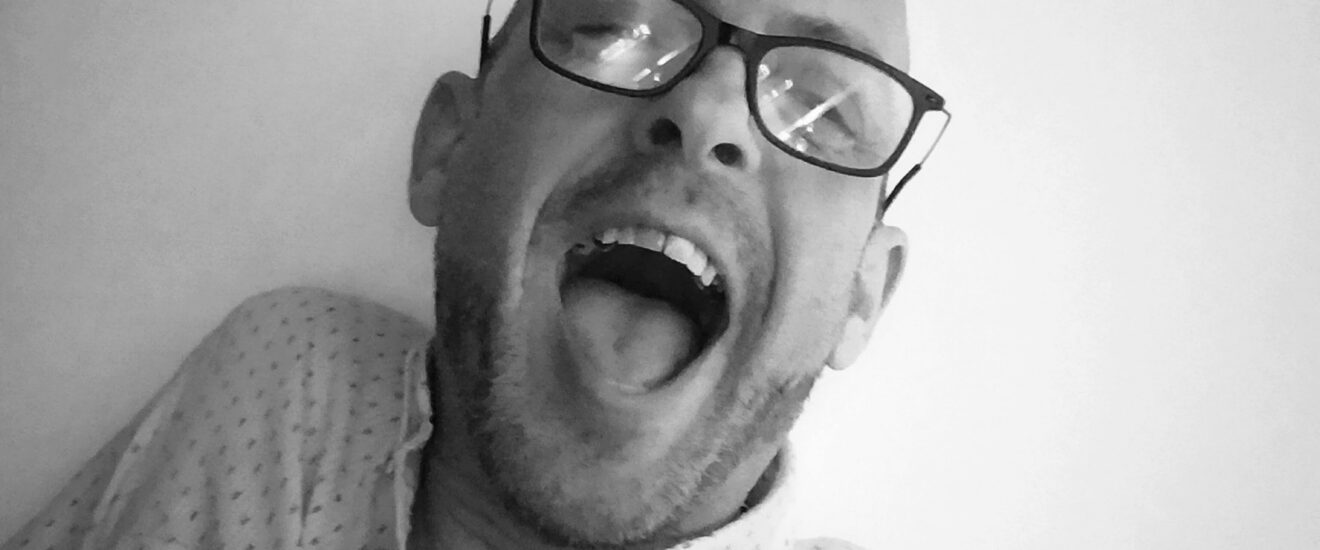 Black and white image of a bald man laughing.
