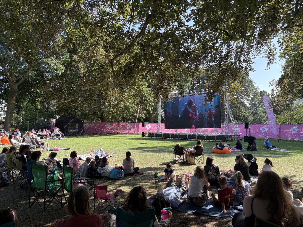 An outdoor cinema, featuring a Large LED screen showing a movie with a crowd gathered around it