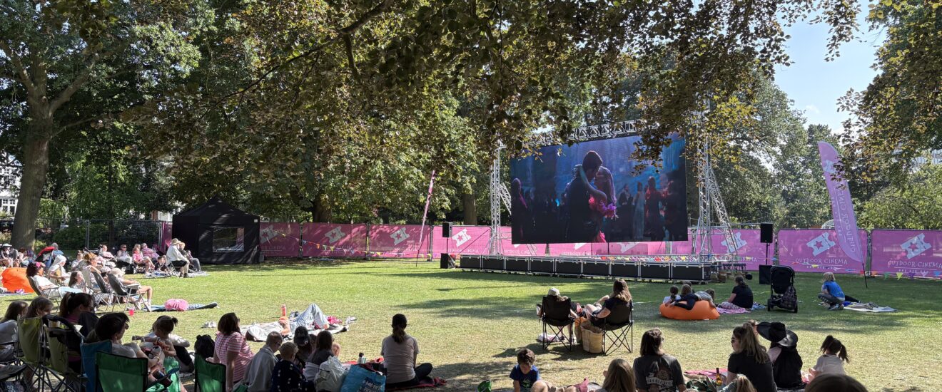 An outdoor cinema, featuring a Large LED screen showing a movie with a crowd gathered around it