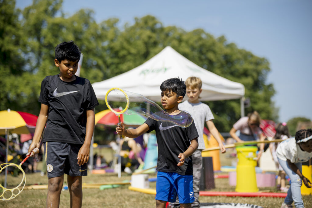 Two children playing with giant bubbles in a park