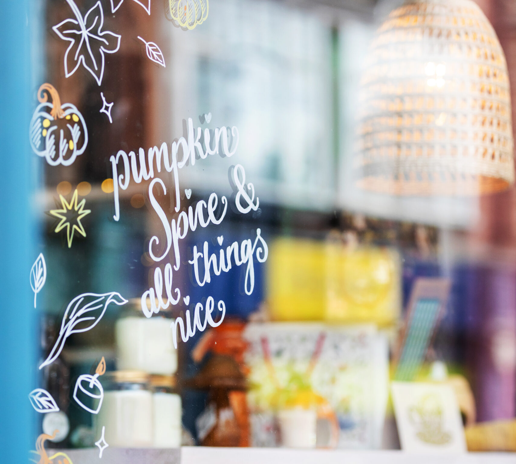 Shop window with hand-painted lettering reading 'Pumpkin spice and all things nice' among an autumn display