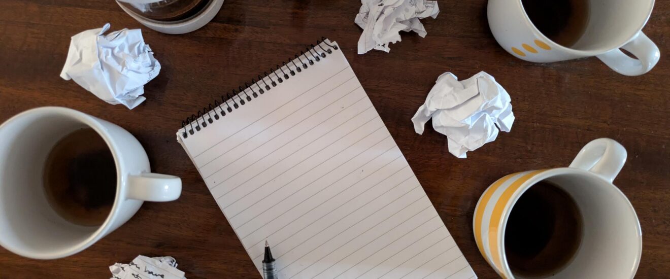 cups of coffee and balled up paper on a wooden table. With a blank notepad in the centre of the image.